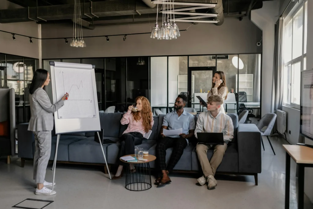 Professional trainer conducting employee sustainability training session with diverse team members in modern office, presenting charts and data on whiteboard
