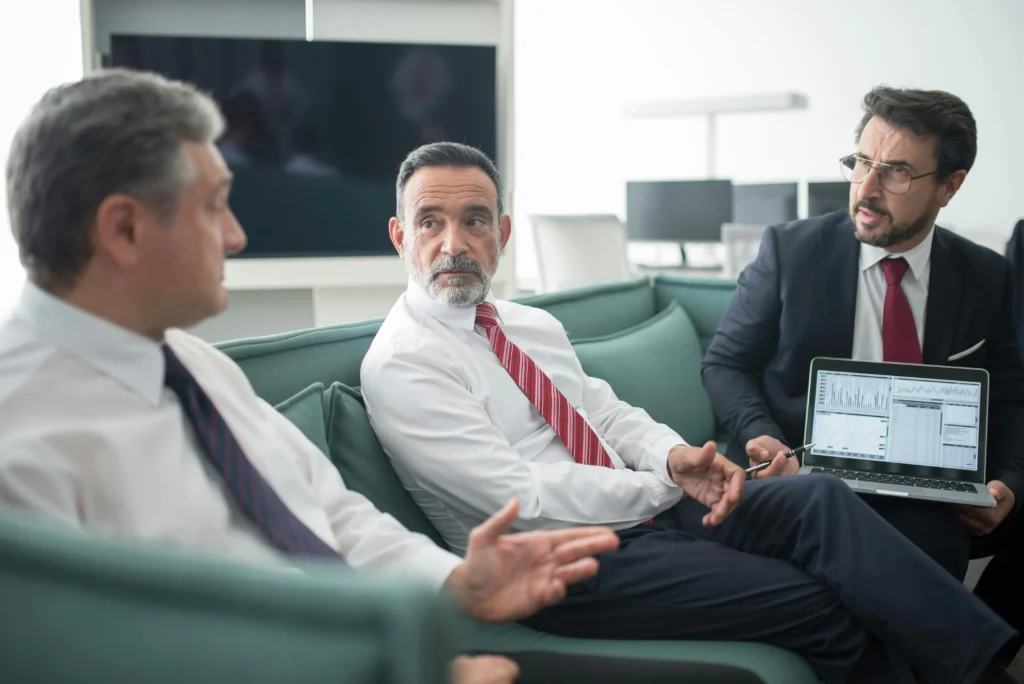Three business executives discussing ethics risk management strategies with laptop and data analysis