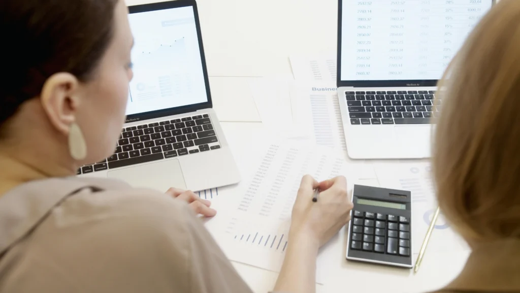 Two professional consultants designing onboarding framework with laptops, documents and calculator