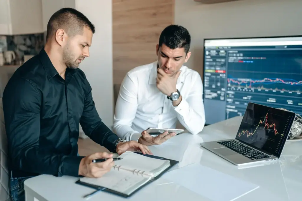 Two business analysts reviewing operational efficiency data and financial charts on multiple screens
