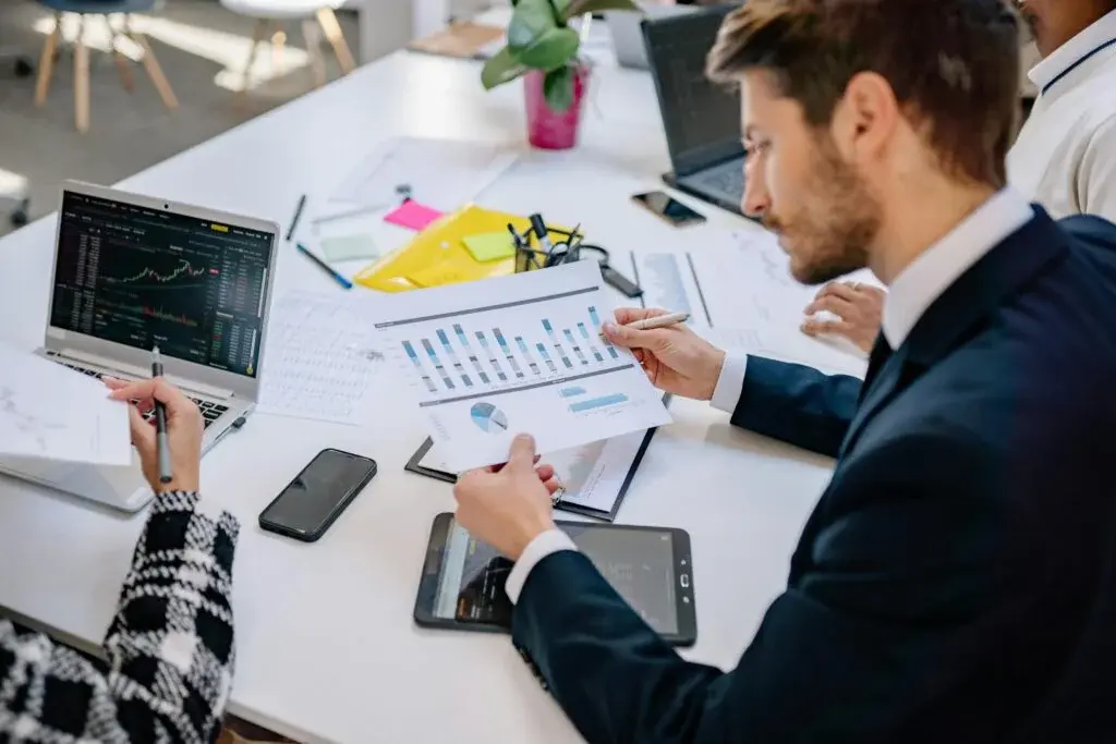 Business professionals conducting post-project evaluation and knowledge transfer session with financial charts and data analysis